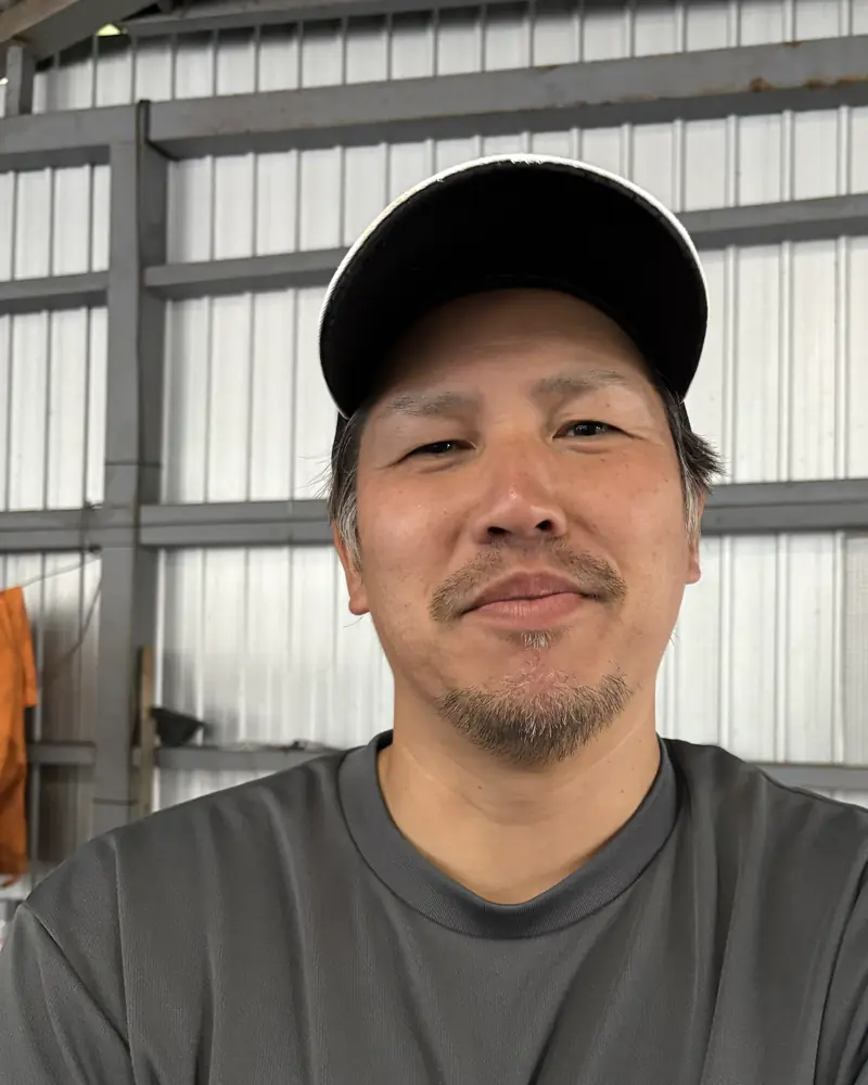 吉川さん。作業小屋で腕を組んで笑顔
